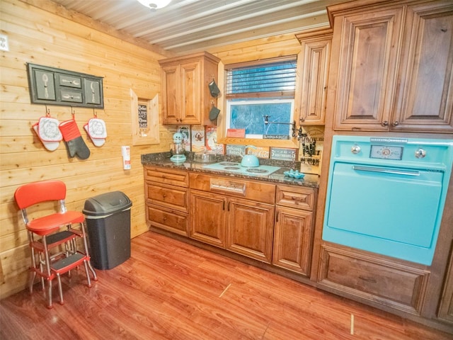 kitchen with wall oven, wooden walls, white electric cooktop, light hardwood / wood-style flooring, and dark stone counters