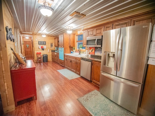 kitchen featuring light hardwood / wood-style flooring, appliances with stainless steel finishes, sink, wooden ceiling, and wood walls