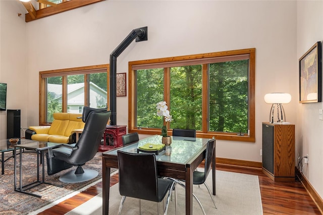 dining space featuring wood-type flooring, a towering ceiling, and a wood stove