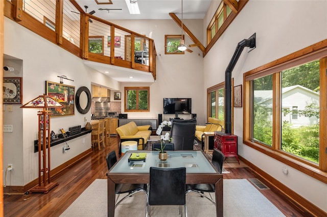 dining area with a towering ceiling, a skylight, a wood stove, dark hardwood / wood-style floors, and ceiling fan