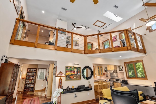 interior space featuring ceiling fan, hardwood / wood-style floors, high vaulted ceiling, and a skylight