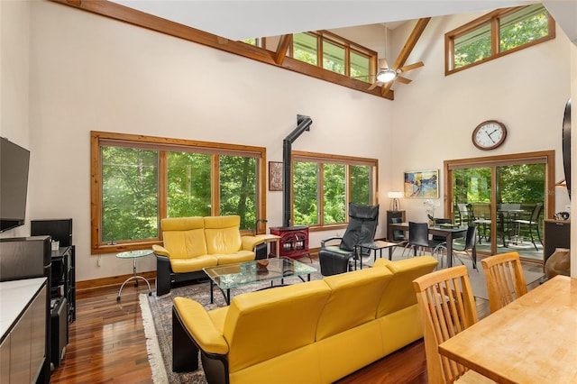 living room with ceiling fan, a high ceiling, a wood stove, and dark hardwood / wood-style flooring