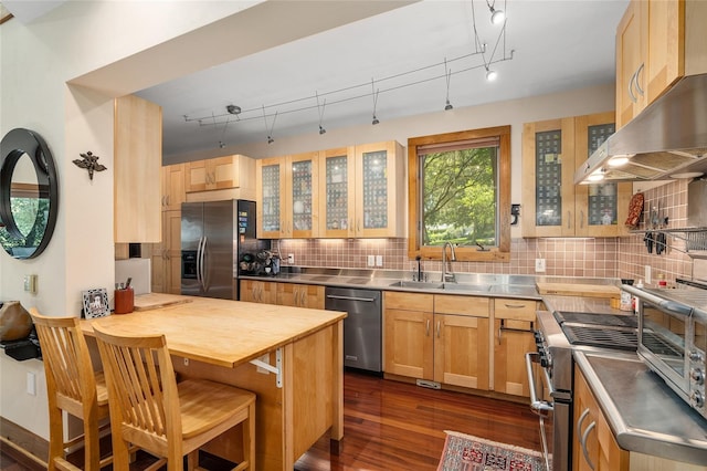 kitchen with appliances with stainless steel finishes, stainless steel counters, tasteful backsplash, sink, and a breakfast bar