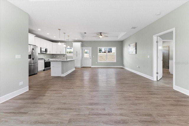 kitchen featuring appliances with stainless steel finishes, decorative light fixtures, white cabinetry, a kitchen island with sink, and ceiling fan