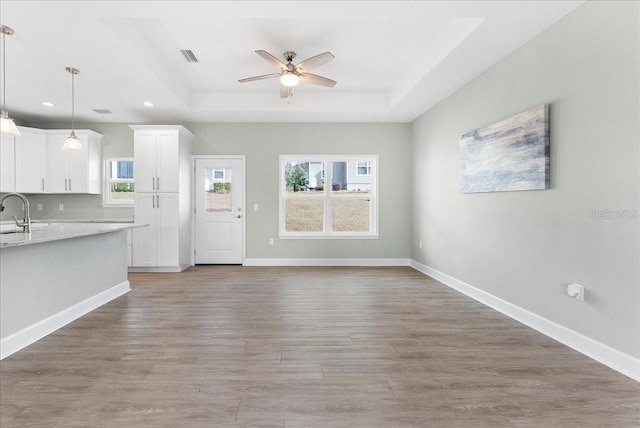 unfurnished living room with wood-type flooring, sink, ceiling fan, and a tray ceiling