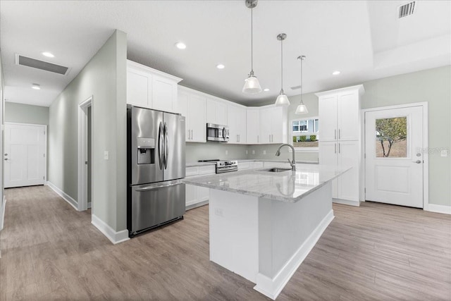 kitchen featuring stainless steel appliances, white cabinetry, a center island with sink, and light stone counters