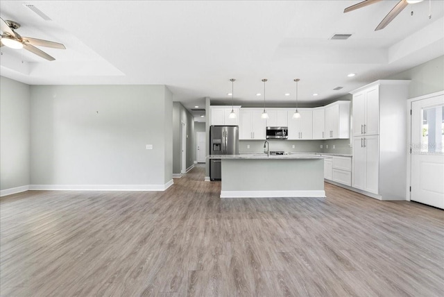 kitchen with light hardwood / wood-style flooring, appliances with stainless steel finishes, white cabinetry, hanging light fixtures, and an island with sink