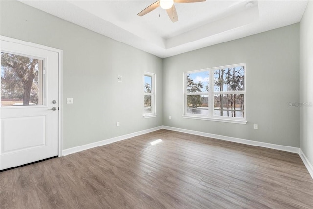 empty room with a raised ceiling, hardwood / wood-style floors, and ceiling fan