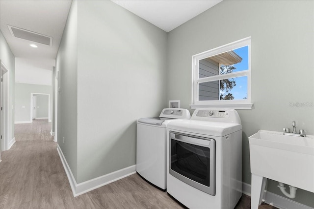 clothes washing area featuring sink, light hardwood / wood-style flooring, and washing machine and dryer