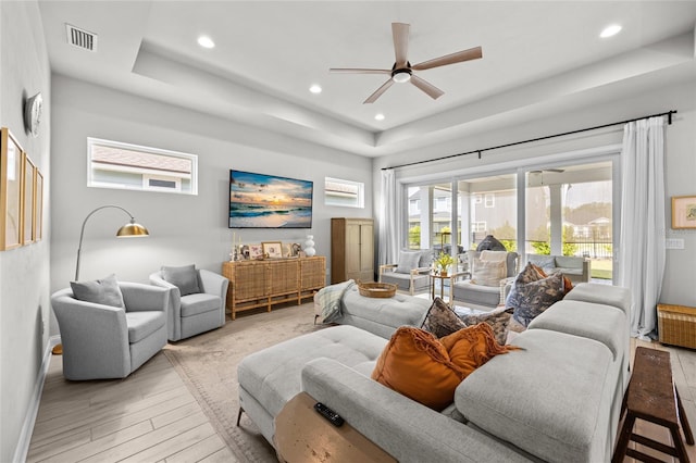 living room with ceiling fan, a raised ceiling, and light hardwood / wood-style floors