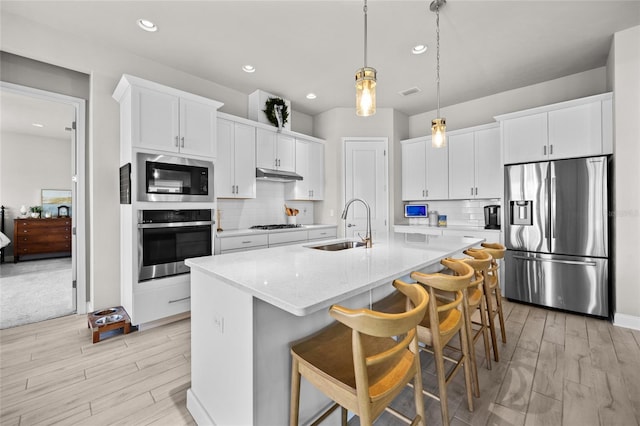 kitchen featuring a kitchen bar, white cabinetry, stainless steel appliances, sink, and a kitchen island with sink