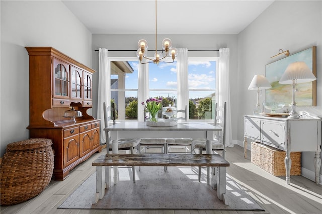 dining area with light wood-type flooring, baseboards, and an inviting chandelier