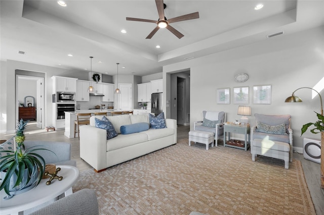 living room with visible vents, recessed lighting, a raised ceiling, and a ceiling fan