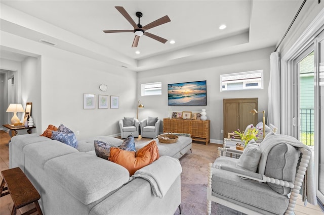 living room featuring a tray ceiling, visible vents, light wood-style floors, and a ceiling fan