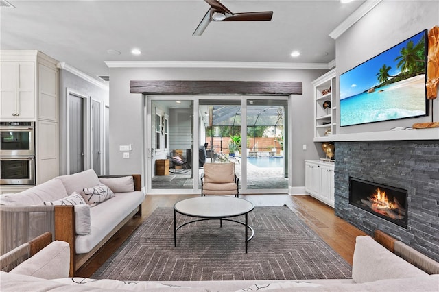 living room with hardwood / wood-style floors, a stone fireplace, ornamental molding, and ceiling fan