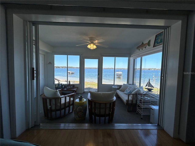 sunroom with ceiling fan and a water view