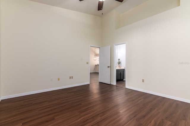 unfurnished bedroom featuring a high ceiling, ensuite bathroom, dark wood-type flooring, and ceiling fan