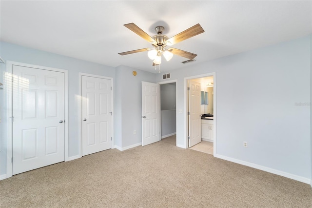 unfurnished bedroom with multiple closets, light carpet, ceiling fan, and ensuite bath