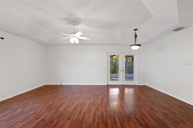 empty room featuring a raised ceiling, dark hardwood / wood-style floors, ceiling fan, and french doors