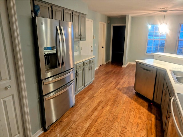 kitchen featuring gray cabinets, decorative light fixtures, sink, stainless steel fridge, and light hardwood / wood-style floors