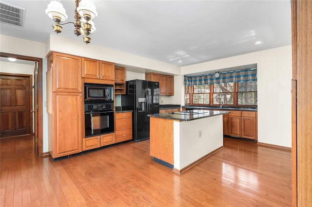 kitchen featuring pendant lighting, a chandelier, a center island, black appliances, and light hardwood / wood-style flooring