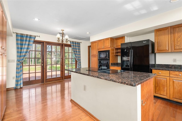 kitchen featuring dark stone countertops, a kitchen island, light hardwood / wood-style flooring, and black appliances