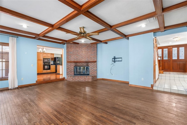 unfurnished living room featuring ceiling fan with notable chandelier, beamed ceiling, wood-type flooring, coffered ceiling, and a brick fireplace