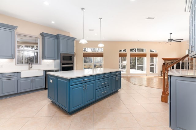 kitchen featuring light tile patterned flooring, blue cabinets, a center island, appliances with stainless steel finishes, and pendant lighting