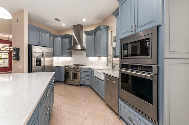 kitchen with wall chimney range hood, sink, appliances with stainless steel finishes, hanging light fixtures, and decorative backsplash