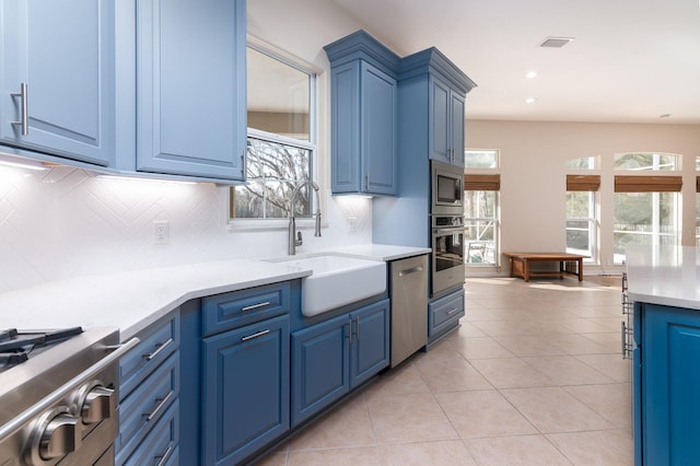 kitchen with sink, light tile patterned floors, appliances with stainless steel finishes, blue cabinets, and decorative backsplash