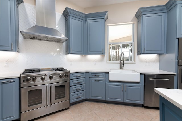 kitchen featuring wall chimney exhaust hood, blue cabinets, sink, appliances with stainless steel finishes, and decorative backsplash