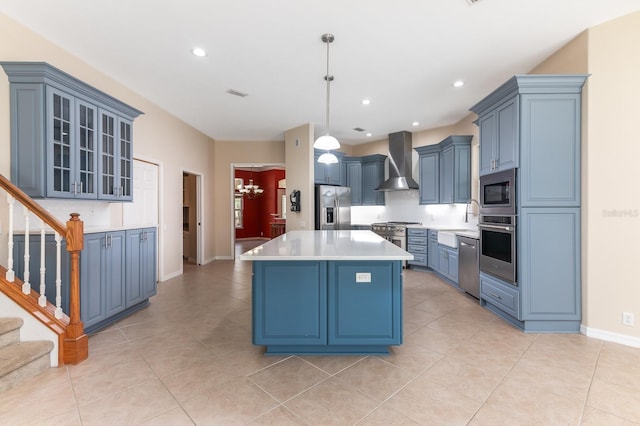 kitchen with wall chimney exhaust hood, blue cabinets, decorative light fixtures, a kitchen island, and stainless steel appliances