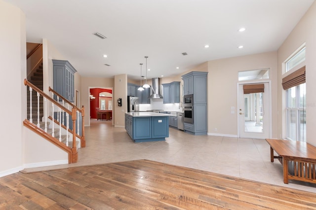 kitchen with a kitchen island, appliances with stainless steel finishes, decorative light fixtures, wall chimney range hood, and light hardwood / wood-style flooring