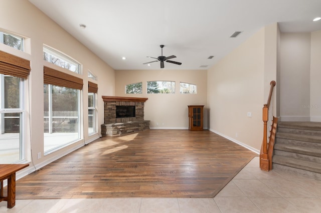 living room featuring ceiling fan, a stone fireplace, and light wood-type flooring