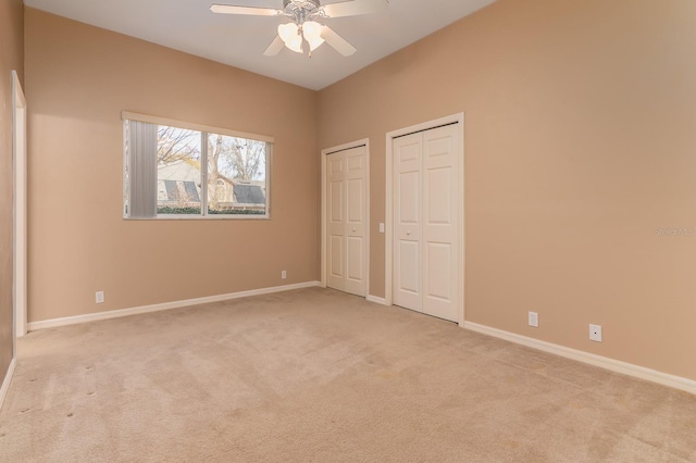 unfurnished bedroom featuring multiple closets, light colored carpet, and ceiling fan