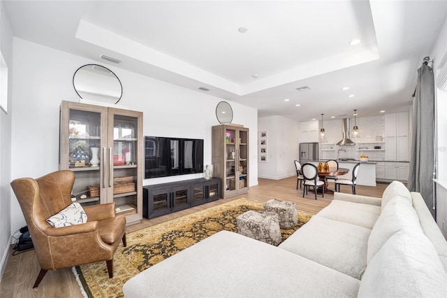 living room with a tray ceiling and light wood-type flooring