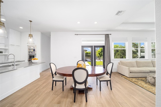 dining space featuring french doors, sink, light wood-type flooring, and a tray ceiling