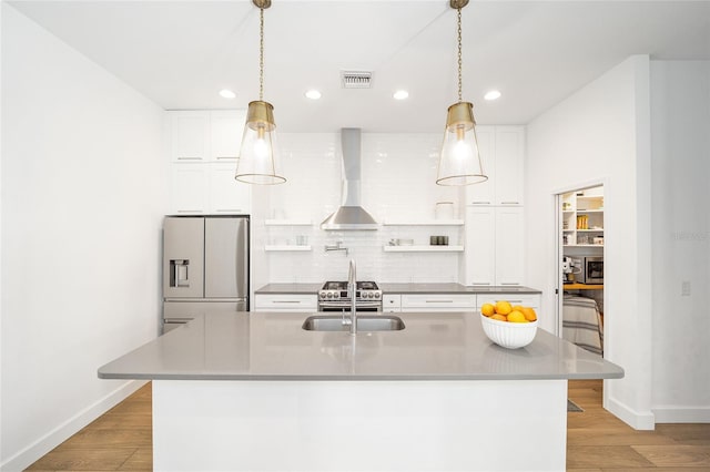 kitchen featuring wall chimney exhaust hood, white cabinetry, a center island with sink, stainless steel appliances, and decorative backsplash