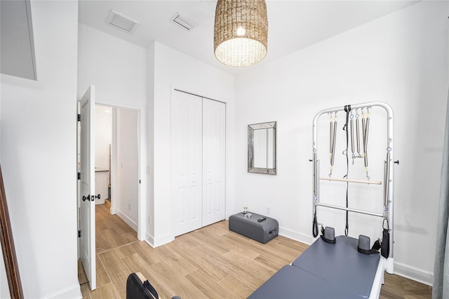 exercise room with a notable chandelier and light wood-type flooring