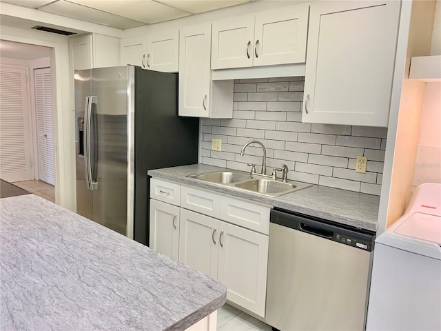 kitchen featuring appliances with stainless steel finishes, white cabinetry, washer / dryer, sink, and light tile patterned floors