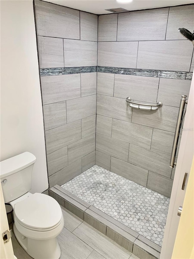 bathroom with a tile shower and toilet