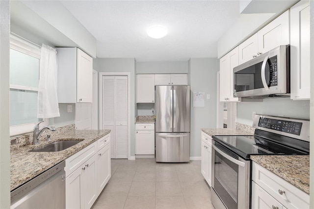 kitchen featuring white cabinetry, sink, light tile patterned floors, light stone counters, and stainless steel appliances