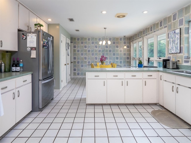 kitchen with tile walls, light tile patterned floors, visible vents, freestanding refrigerator, and white cabinets