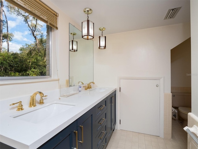 bathroom featuring toilet, double vanity, a sink, and visible vents