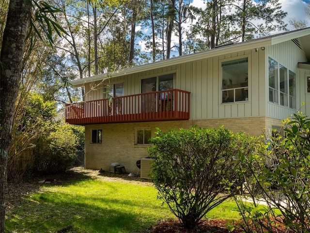 rear view of property featuring brick siding, a yard, central air condition unit, board and batten siding, and a balcony