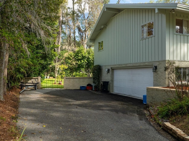 view of side of property with a garage, fence, board and batten siding, and brick siding