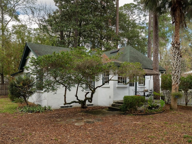 view of side of property with a shingled roof, fence, and stucco siding