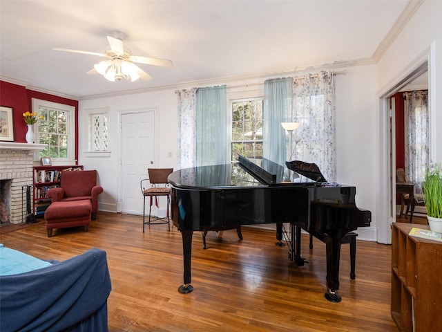 sitting room with ornamental molding, a fireplace, ceiling fan, and wood finished floors