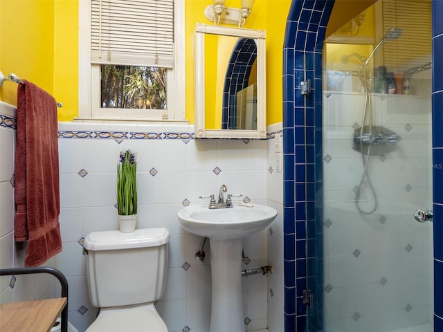 bathroom featuring toilet, a stall shower, tile walls, and a sink