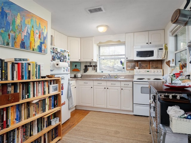 kitchen with visible vents, light wood-style floors, white cabinets, a sink, and white appliances